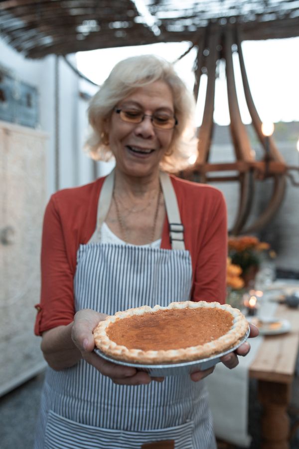 A smiling elderly woman holding a pumpkin pie | Source: Pexels