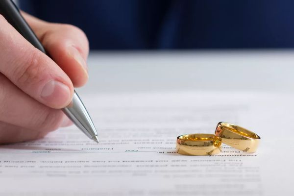 A person signing divorce papers with two gold rings nearby