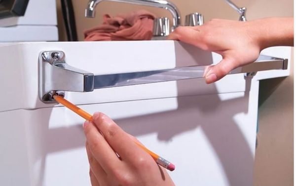 Someone attaching a towel rack to the outside of a laundry sink.